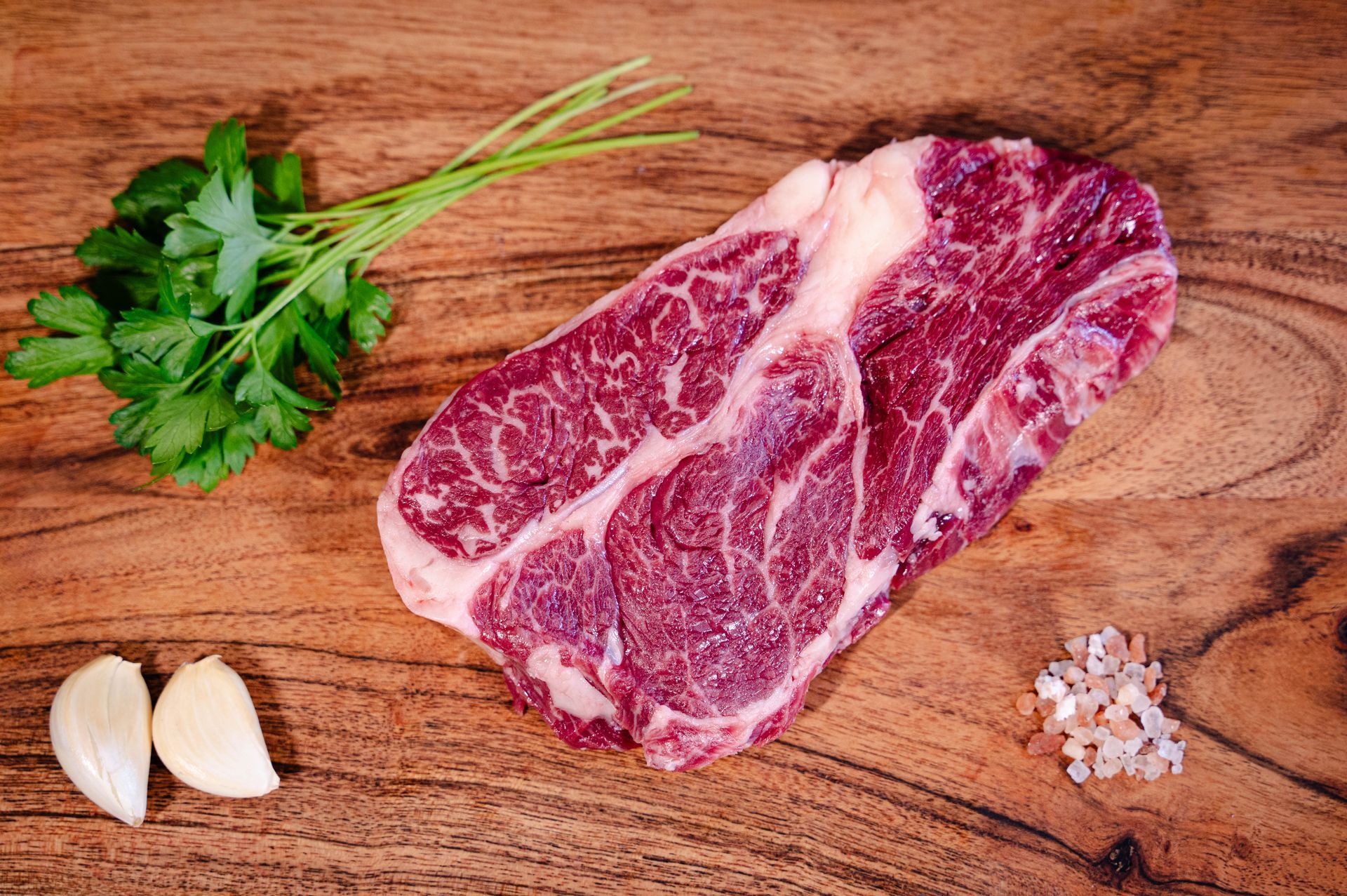 American Wagyu raw chuck eye steak on a cutting board with spices and herbs