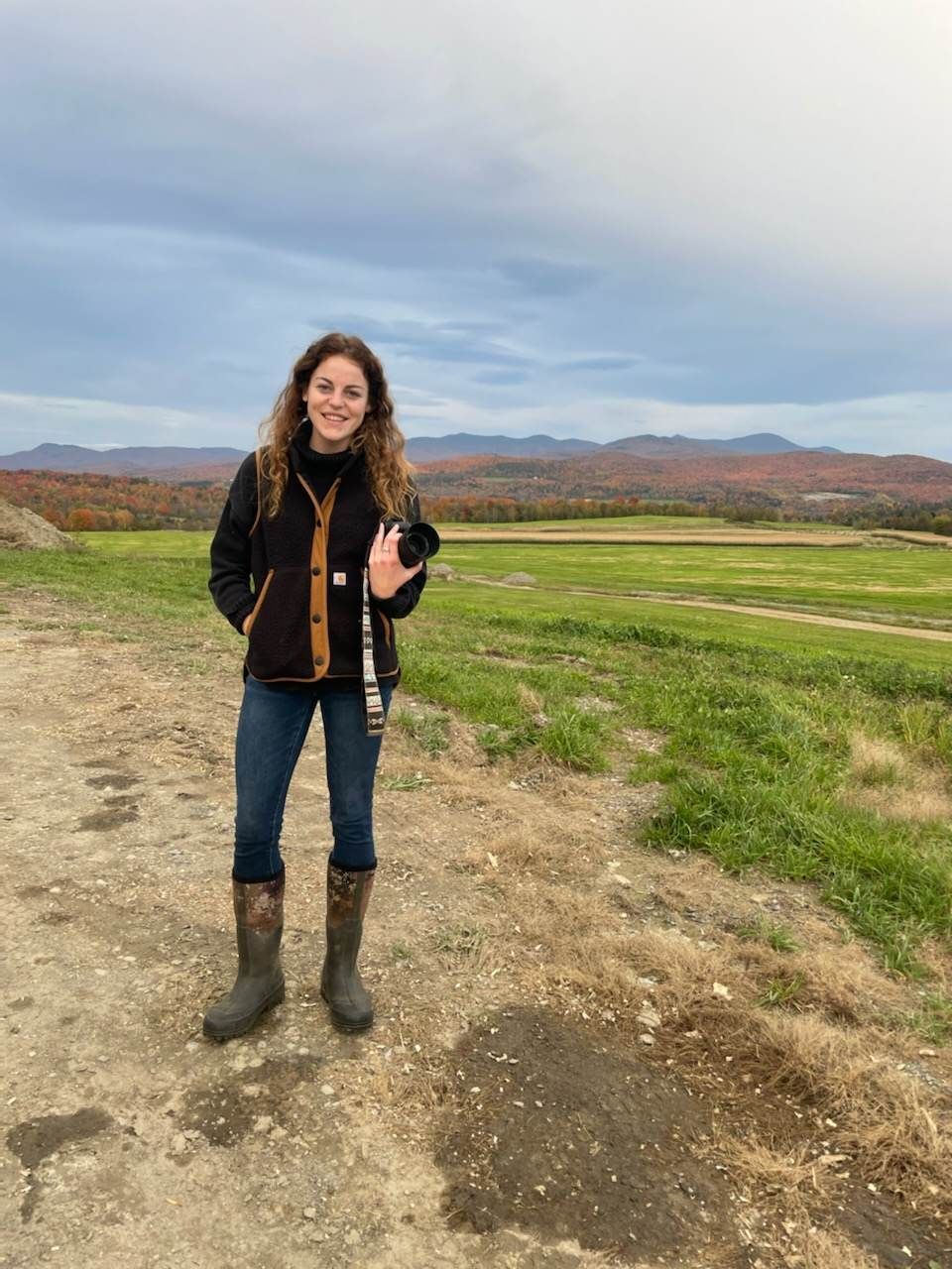 Jenne Hull marketing and communications, holding her camera in a grass field.