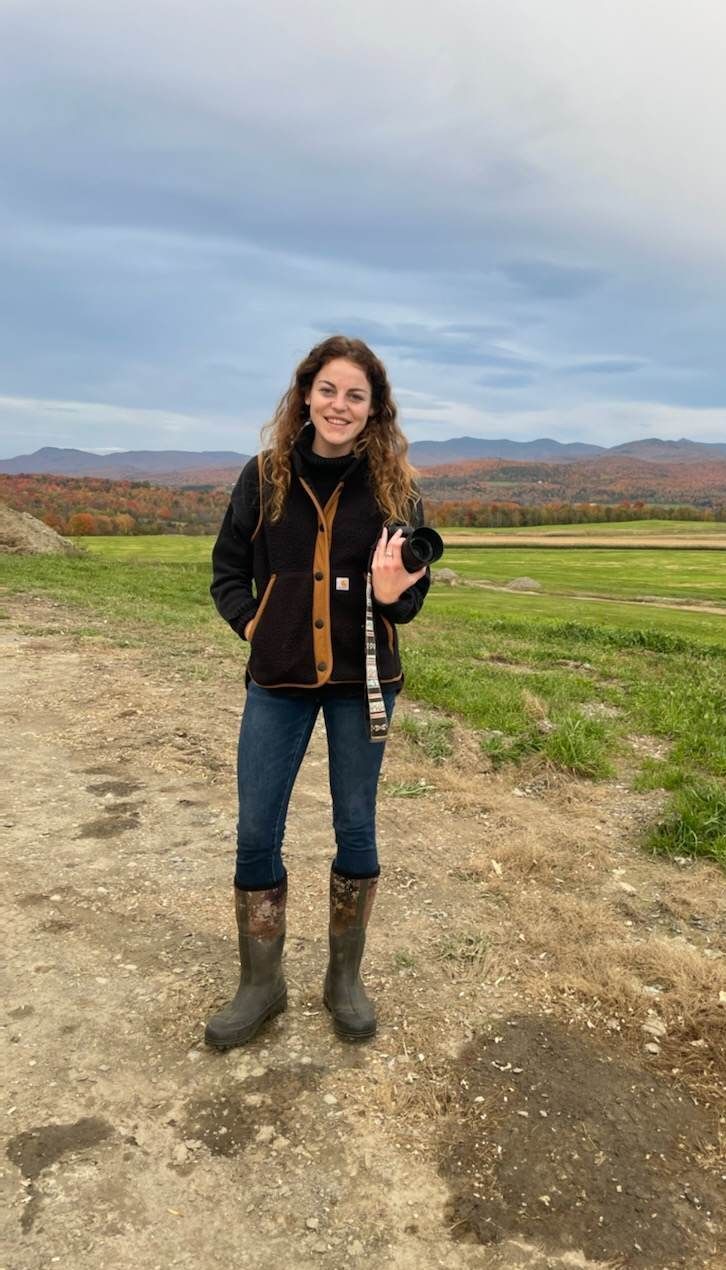 Jenne Hull marketing and communications, holding her camera in a grass field.