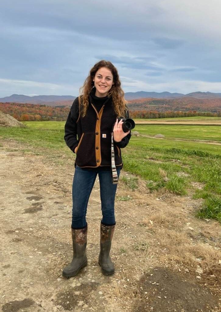 Jenne Hull marketing and communications, holding her camera in a grass field.