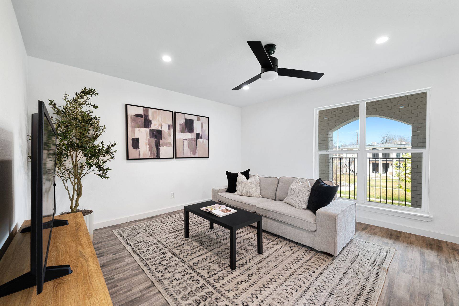 Bright modern living room with gray sofa, black coffee table, large rug, TV stand, and balcony doors.