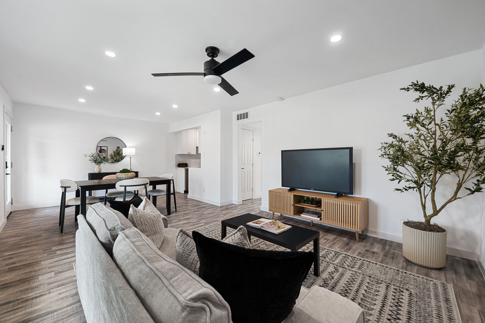 Bright modern living room with gray sectional, TV, dining table, and potted tree