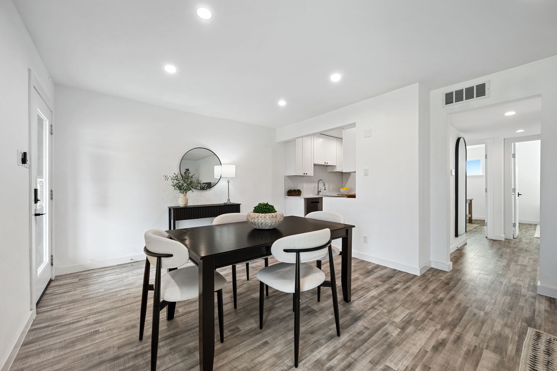 Bright open dining area with black table, white chairs, wood floors, and kitchen in background