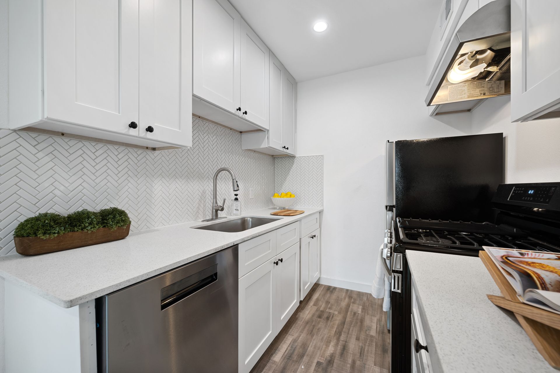 Bright white galley kitchen with stainless appliances, white cabinets, and gray herringbone backsplash.