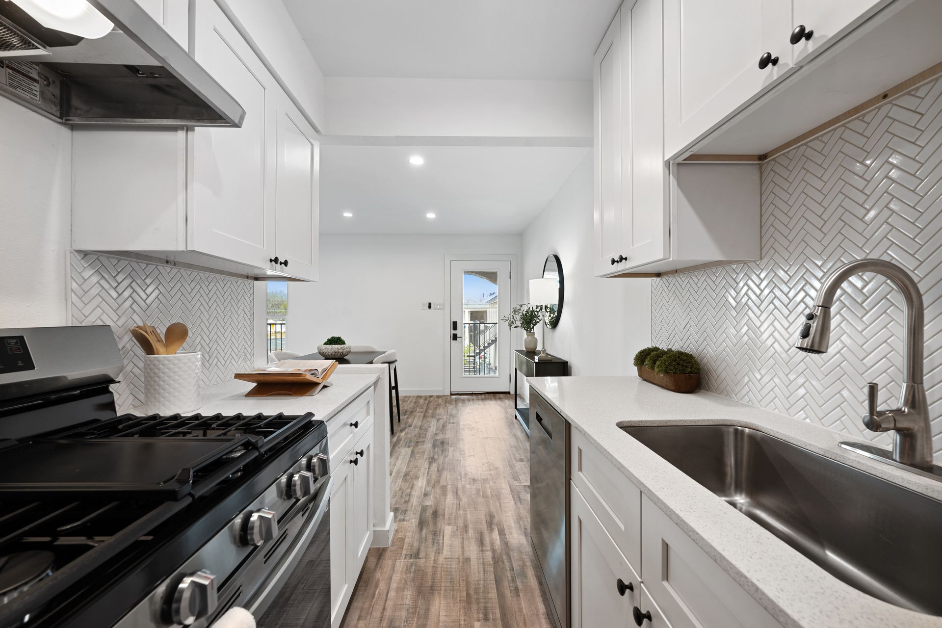 Bright white galley kitchen with black stove, wood floor, and stainless sink and faucet