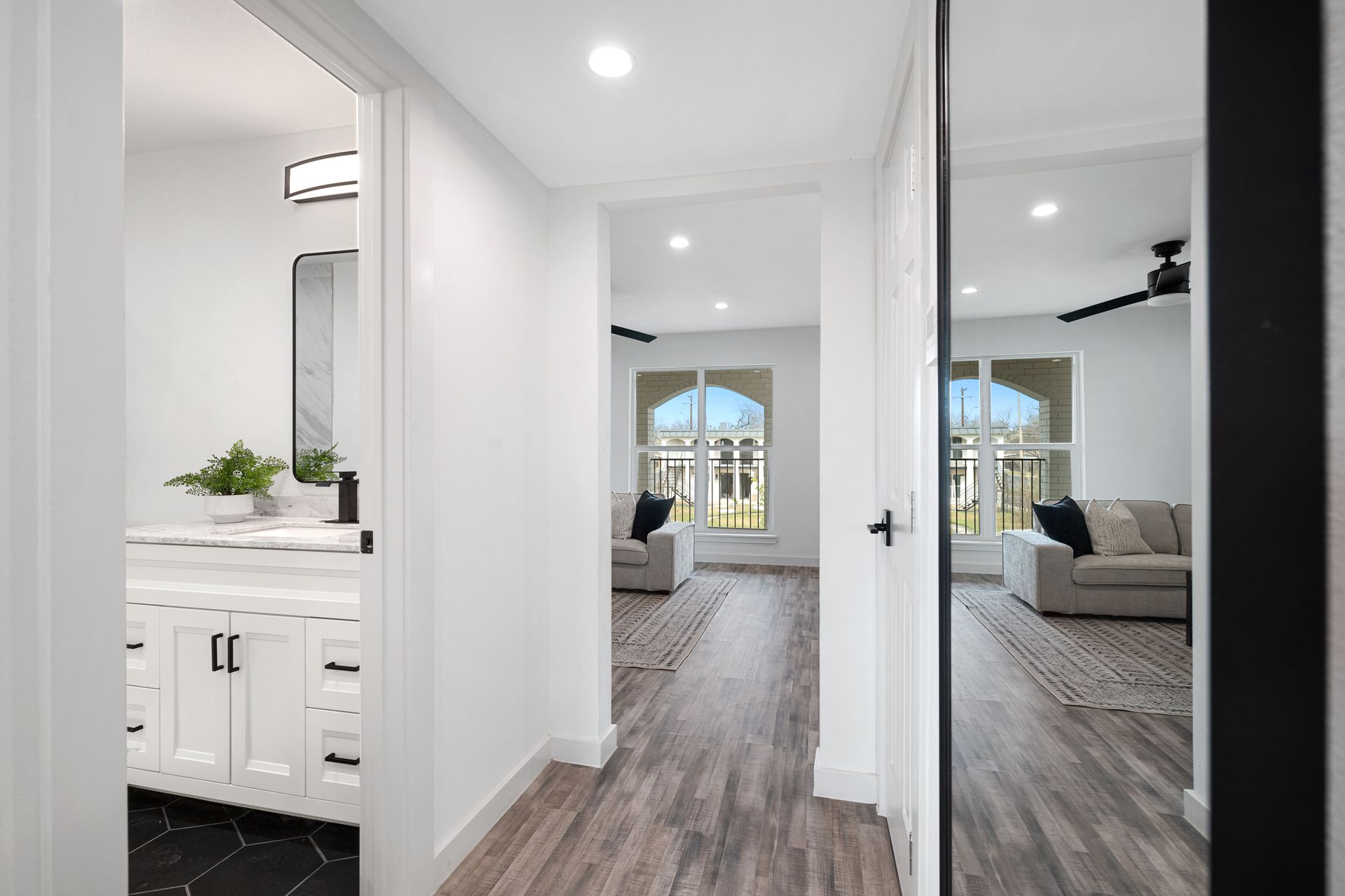 Bright modern hallway with white walls, wood floors, and a view into a bedroom and bathroom