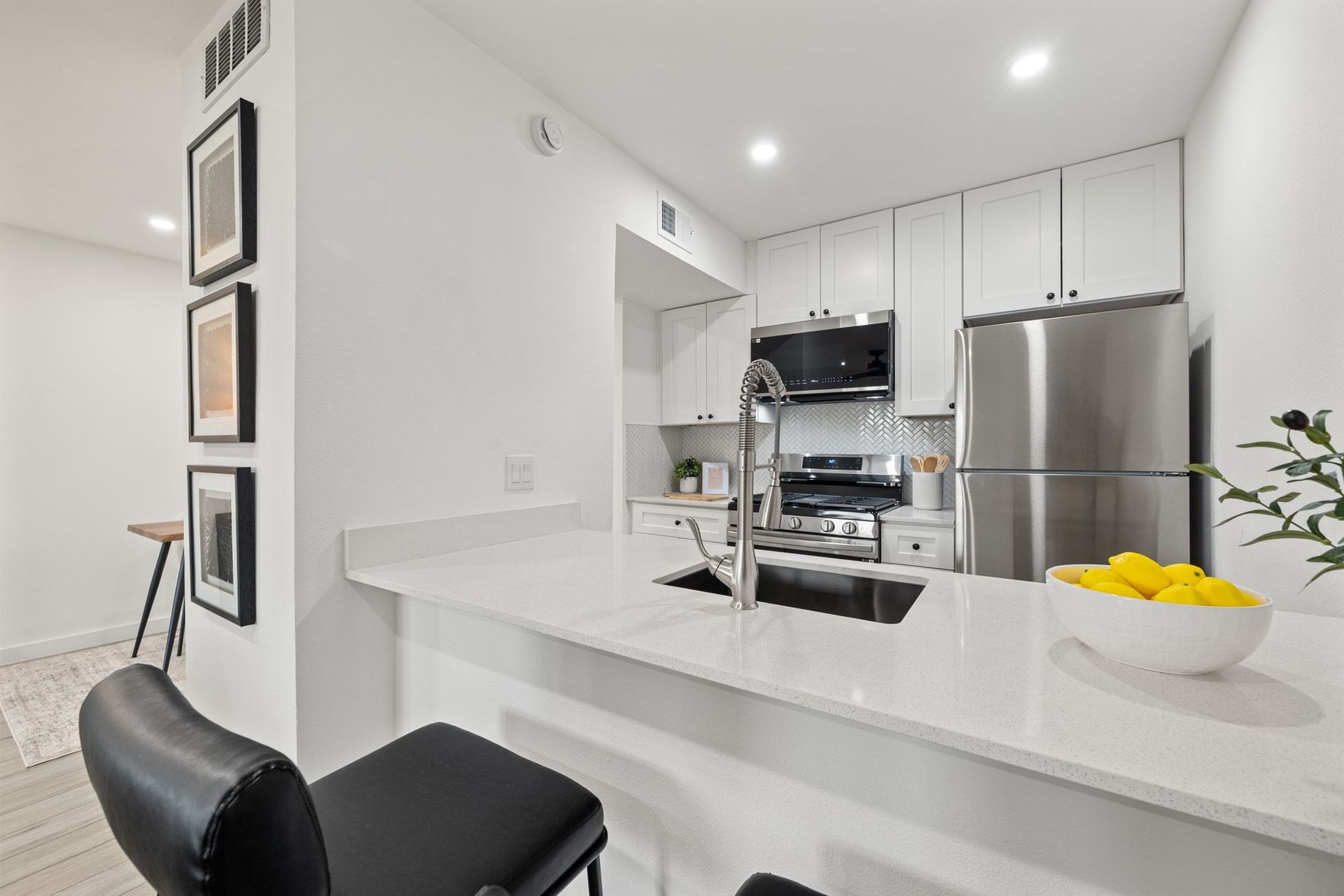 Modern white kitchen with stainless steel appliances, island counter, and bowl of lemons