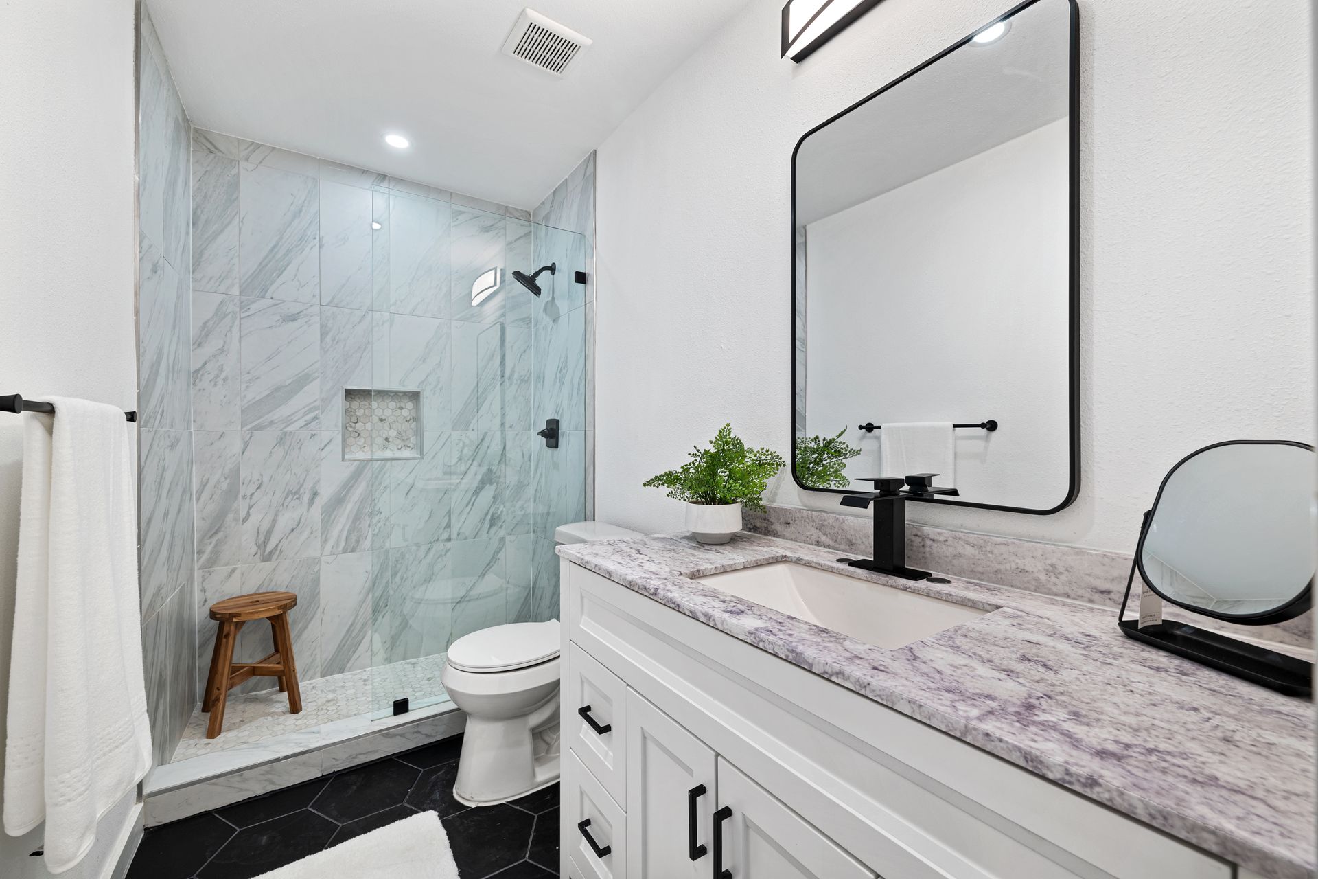 Bright modern bathroom with marble shower, white vanity, large mirror, and black fixtures