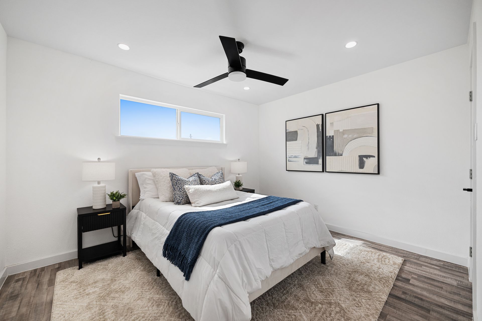 Bright modern bedroom with a bed, ceiling fan, nightstand, and wall art