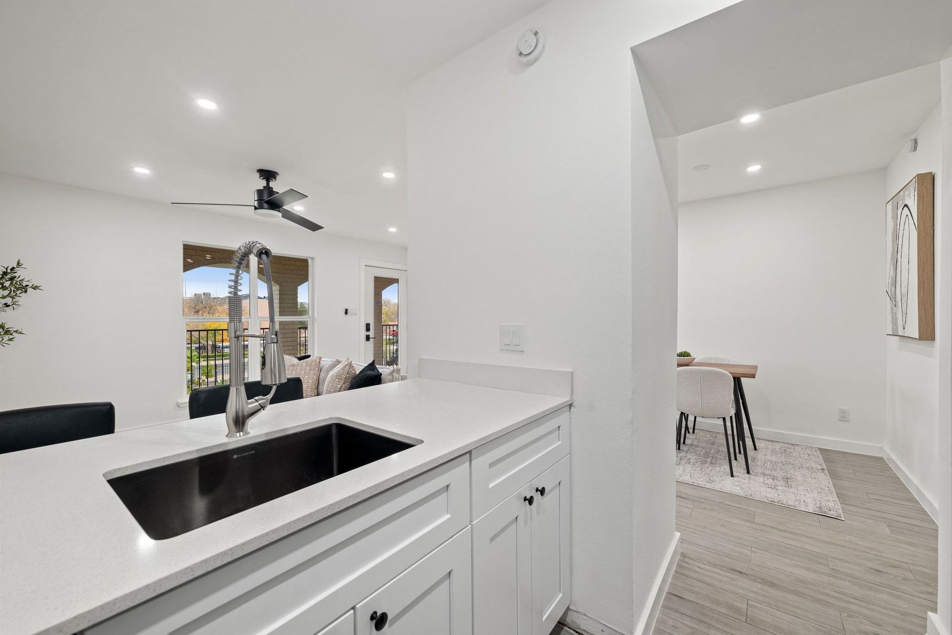 Bright open kitchen with white cabinets, black sink, and view into a small dining area with large windows
