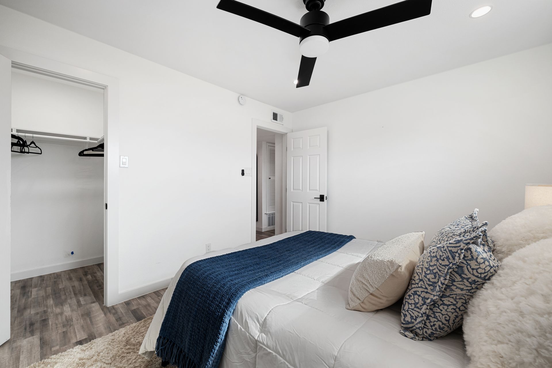 Bright bedroom with white walls, black ceiling fan, bed, and open closet on the left