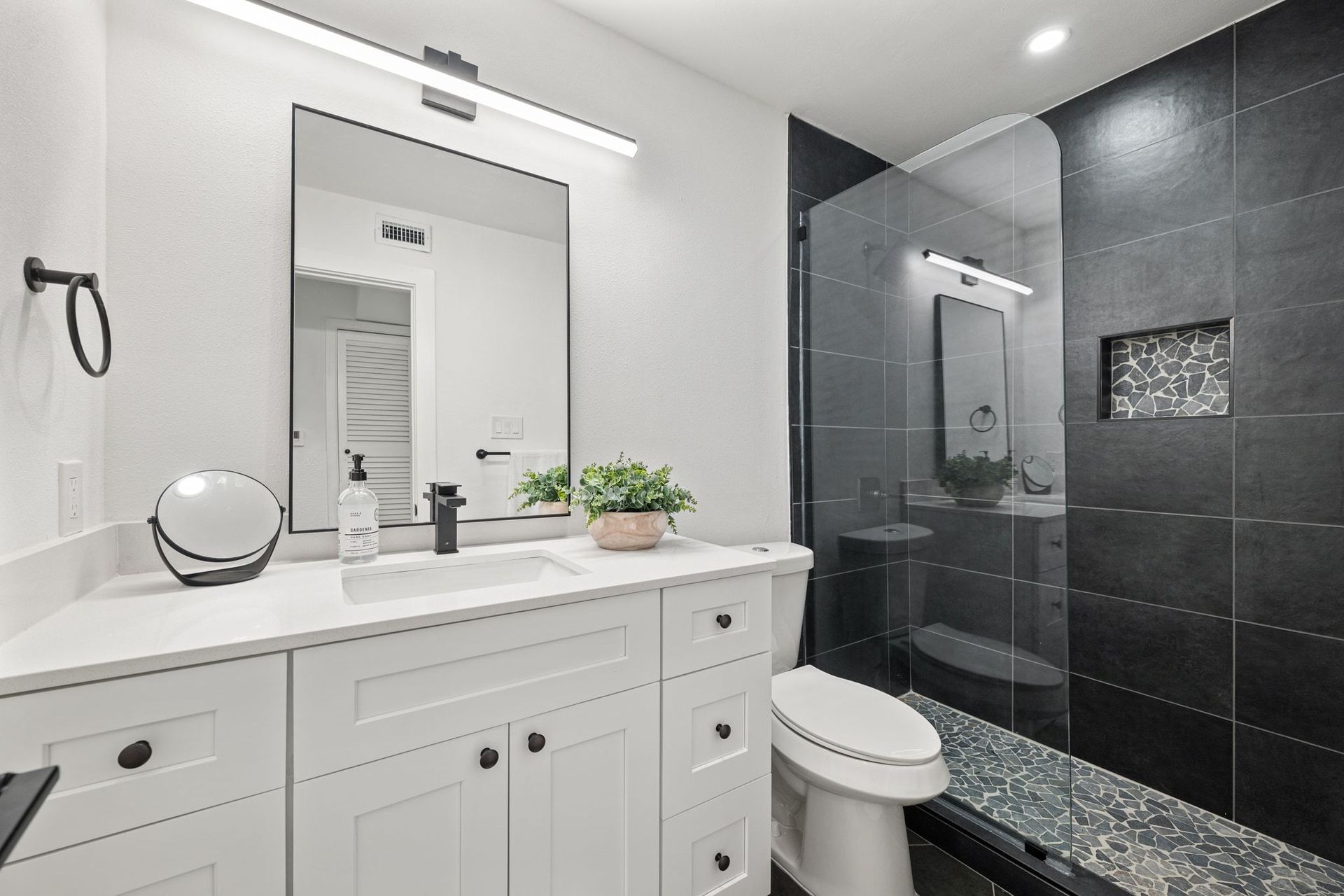 Modern bathroom with white vanity, mirror, and black tiled shower with glass door