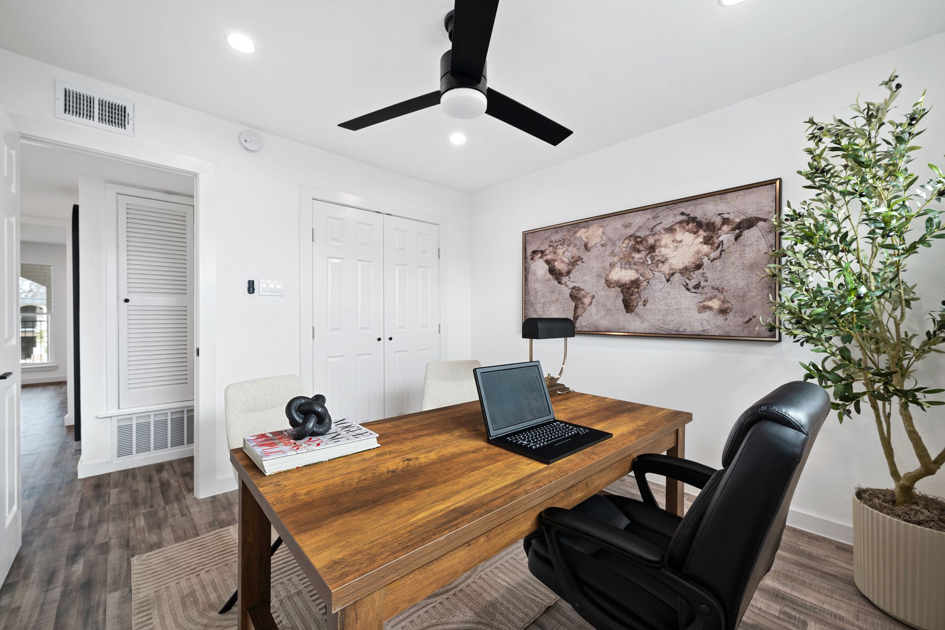 Bright home office with wood desk, black chair, laptop, wall map, and ceiling fan