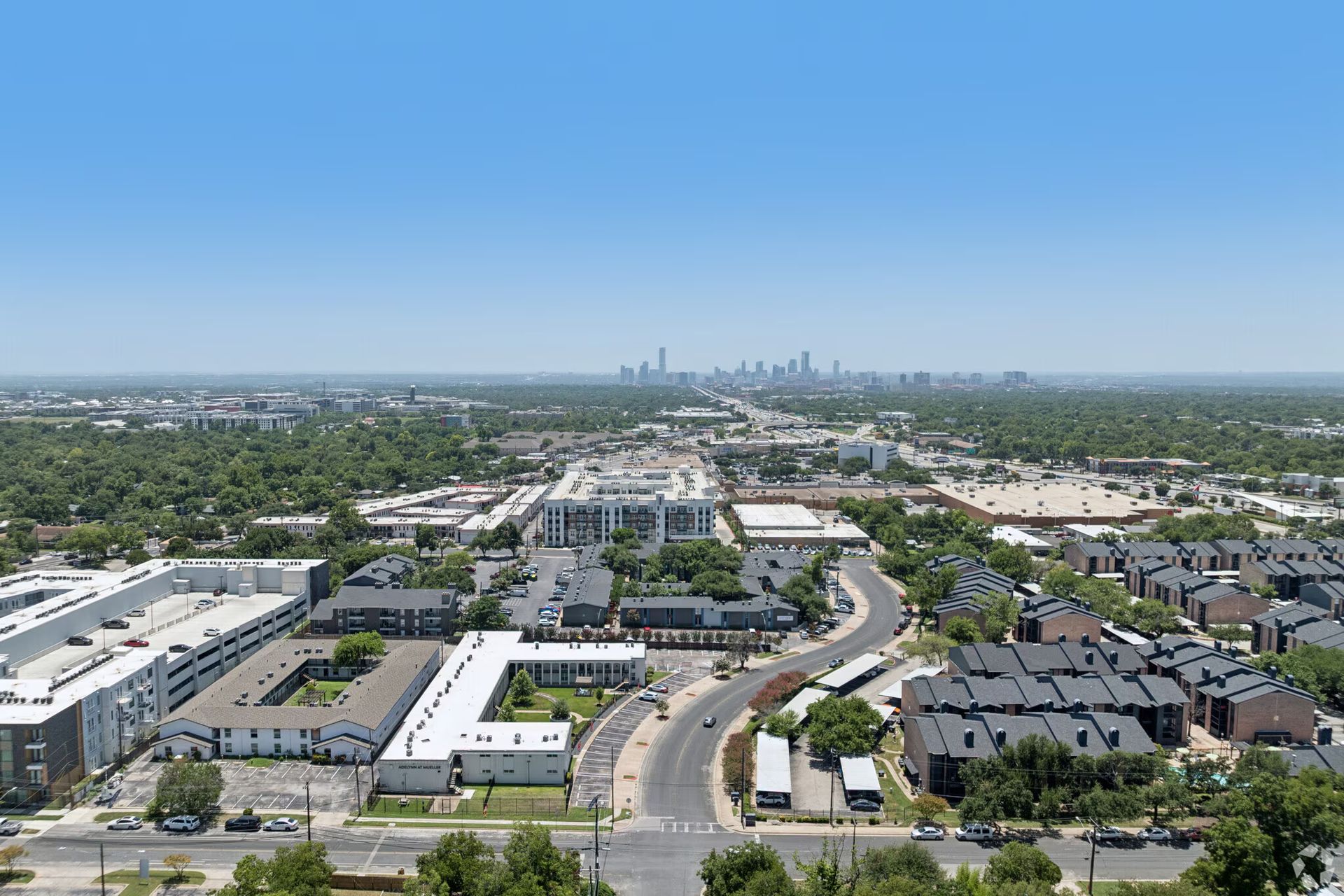 Aerial view of suburban neighborhood with curving roads and distant city skyline under a clear blue sky
