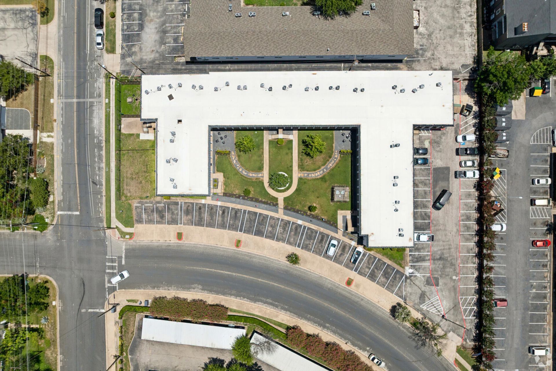 Aerial view of a large white building with parking lots, curved road, and landscaped courtyard.