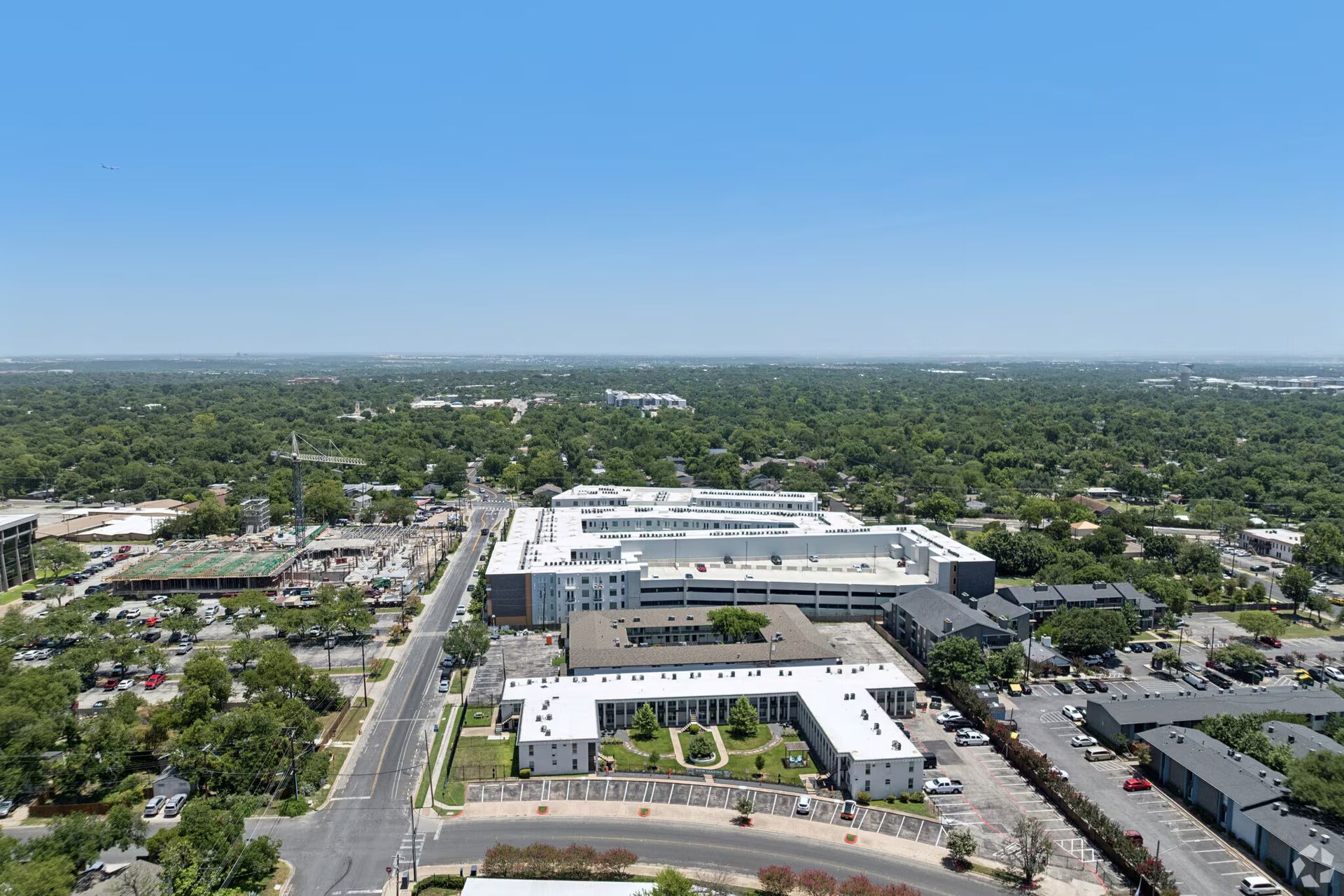 Aerial view of a large white office complex amid suburban greenery under a clear blue sky.