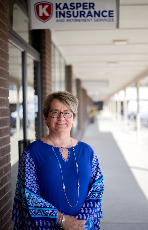 Woman in blue standing outside Kasper Insurance storefront, smiling in a covered walkway.