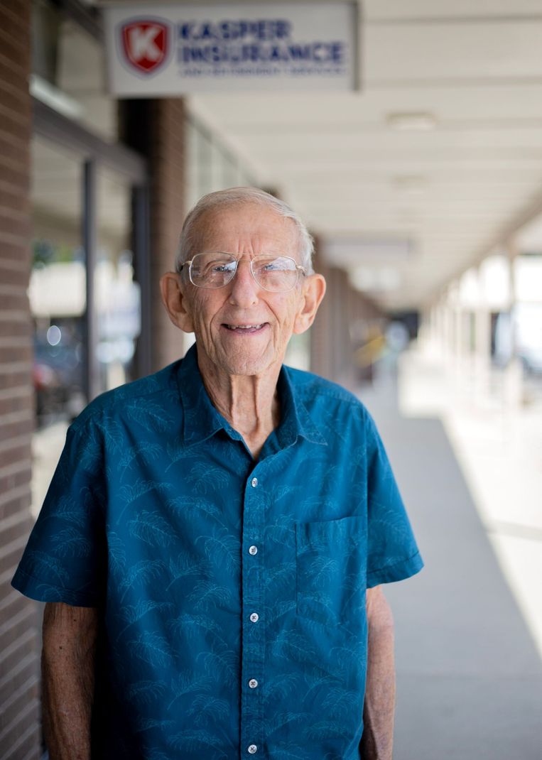 Smiling older man in a blue shirt standing on a covered sidewalk outside a business