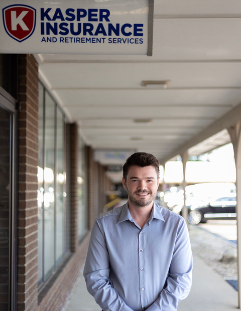 Man standing under a covered walkway outside Kasper Insurance, wearing a light blue shirt and smiling.