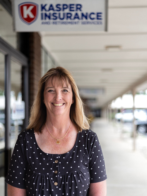 Woman smiling in a hallway beneath a Kasper Insurance sign.