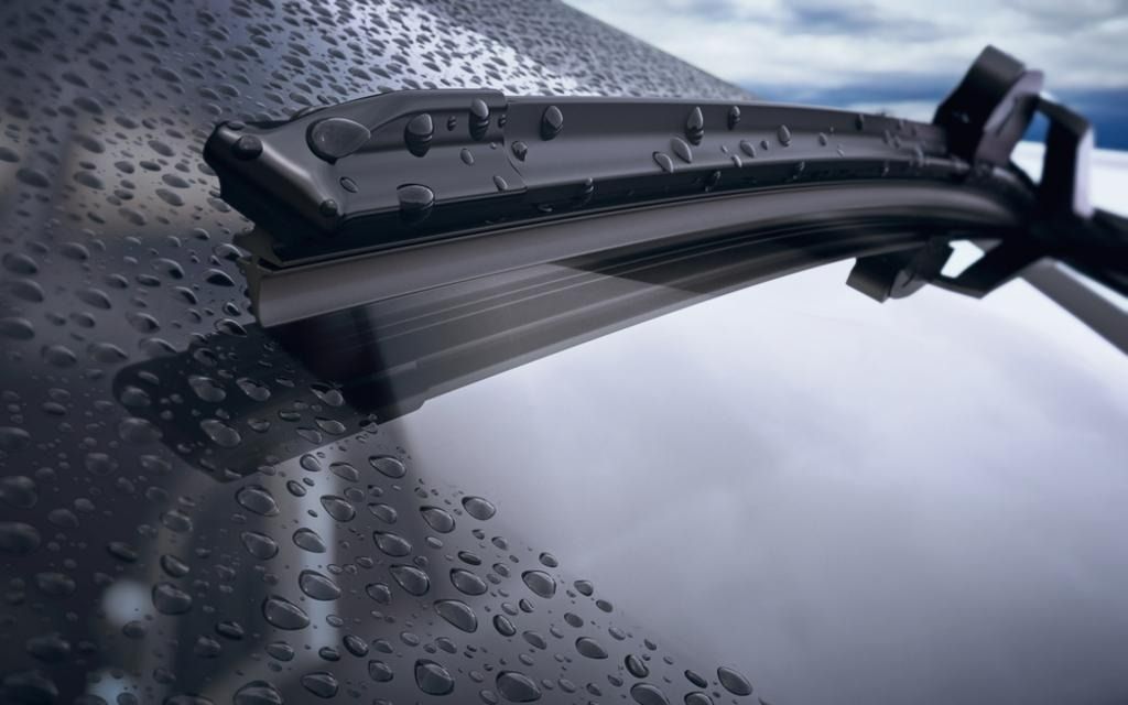 Windshield wiper on a wet car window with water droplets.