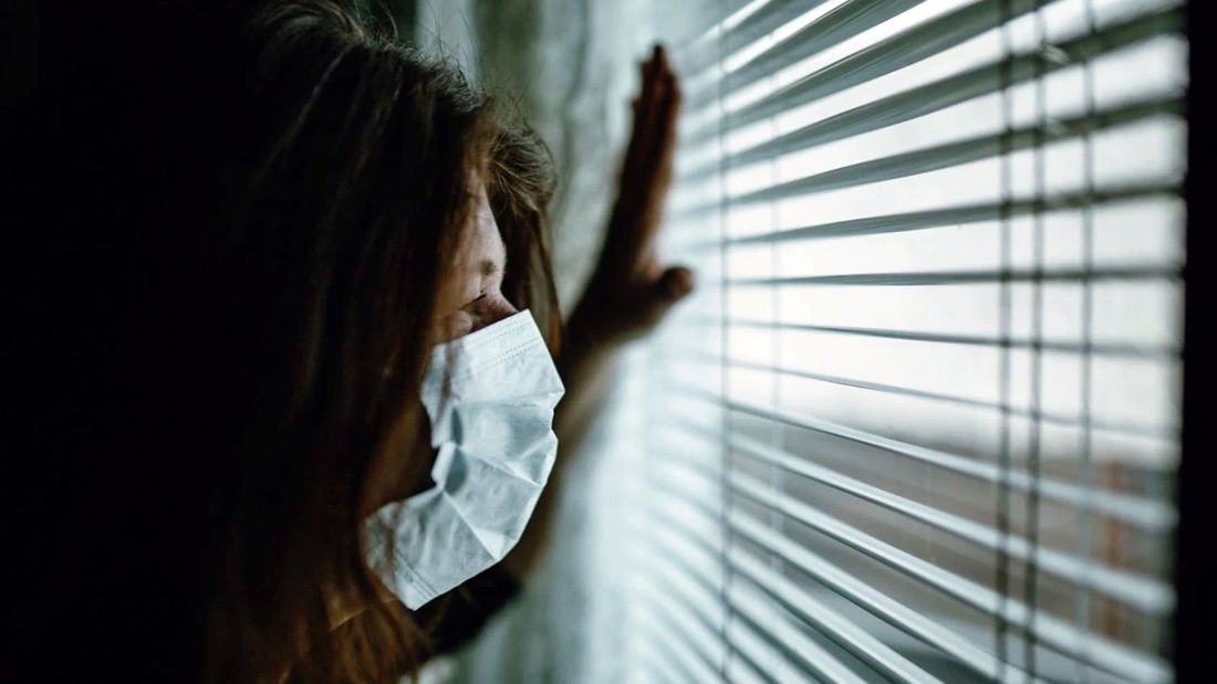 donna con sguardo preoccupato da dietro una finestra