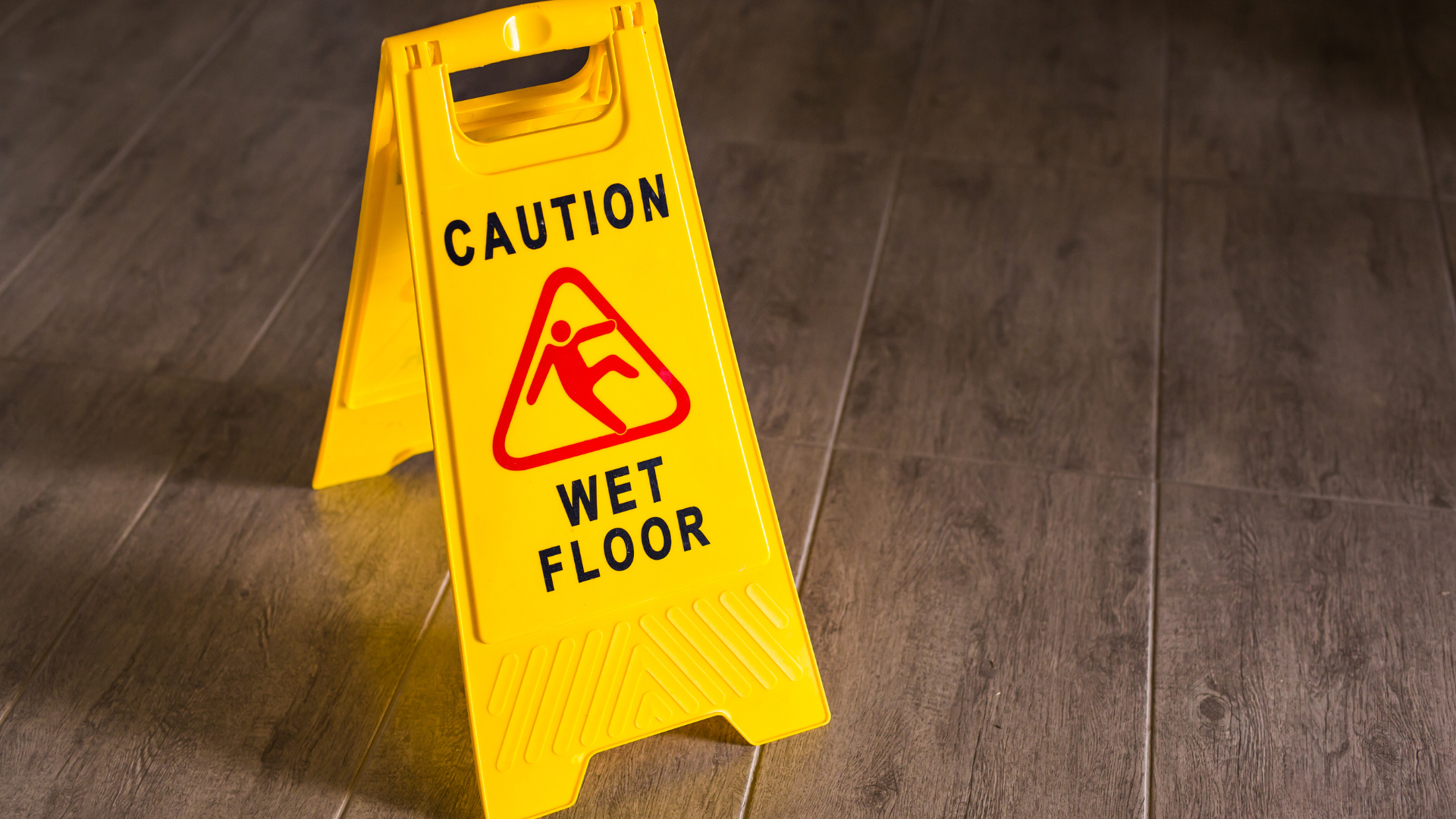 Yellow caution sign warning of wet floor on a dark indoor surface.