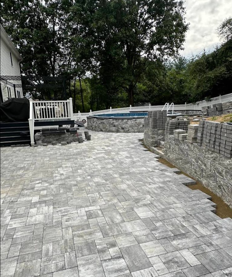 Patio with gray pavers, retaining wall, and pool under construction.
