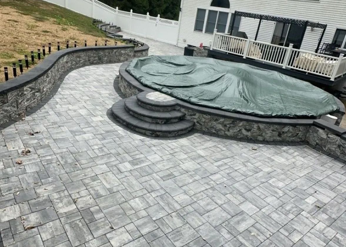 Stone patio surrounds a pool with a cover, steps, and a stone retaining wall.