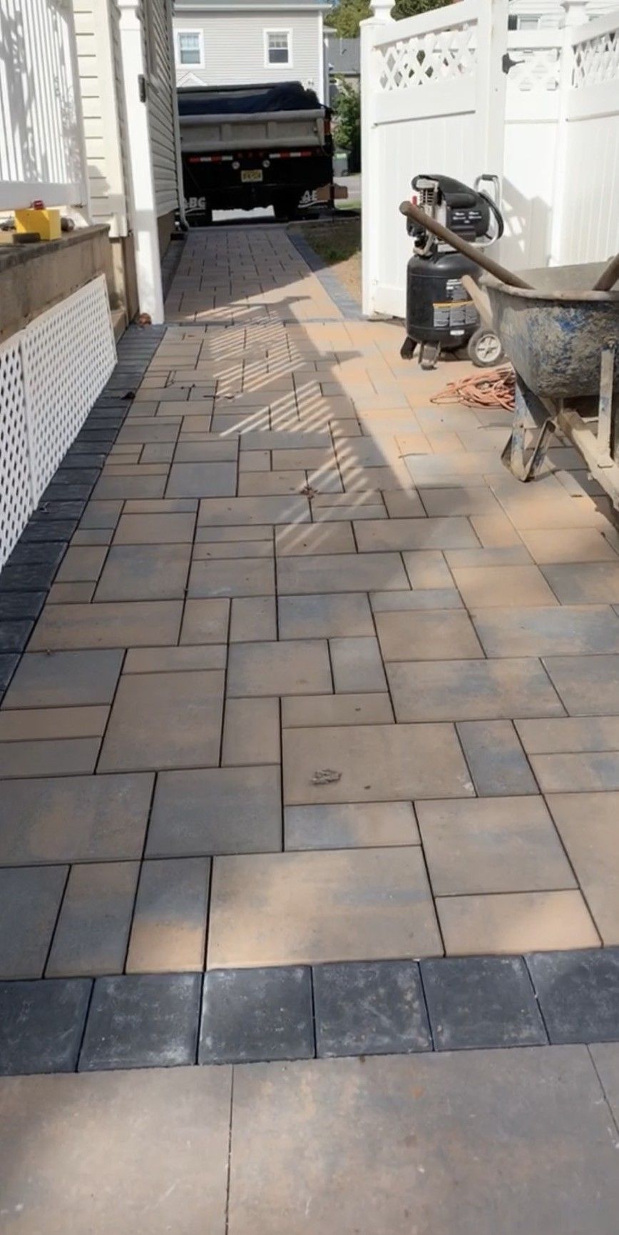 A paved walkway with rectangular pavers, a black border, and a truck in the distance.