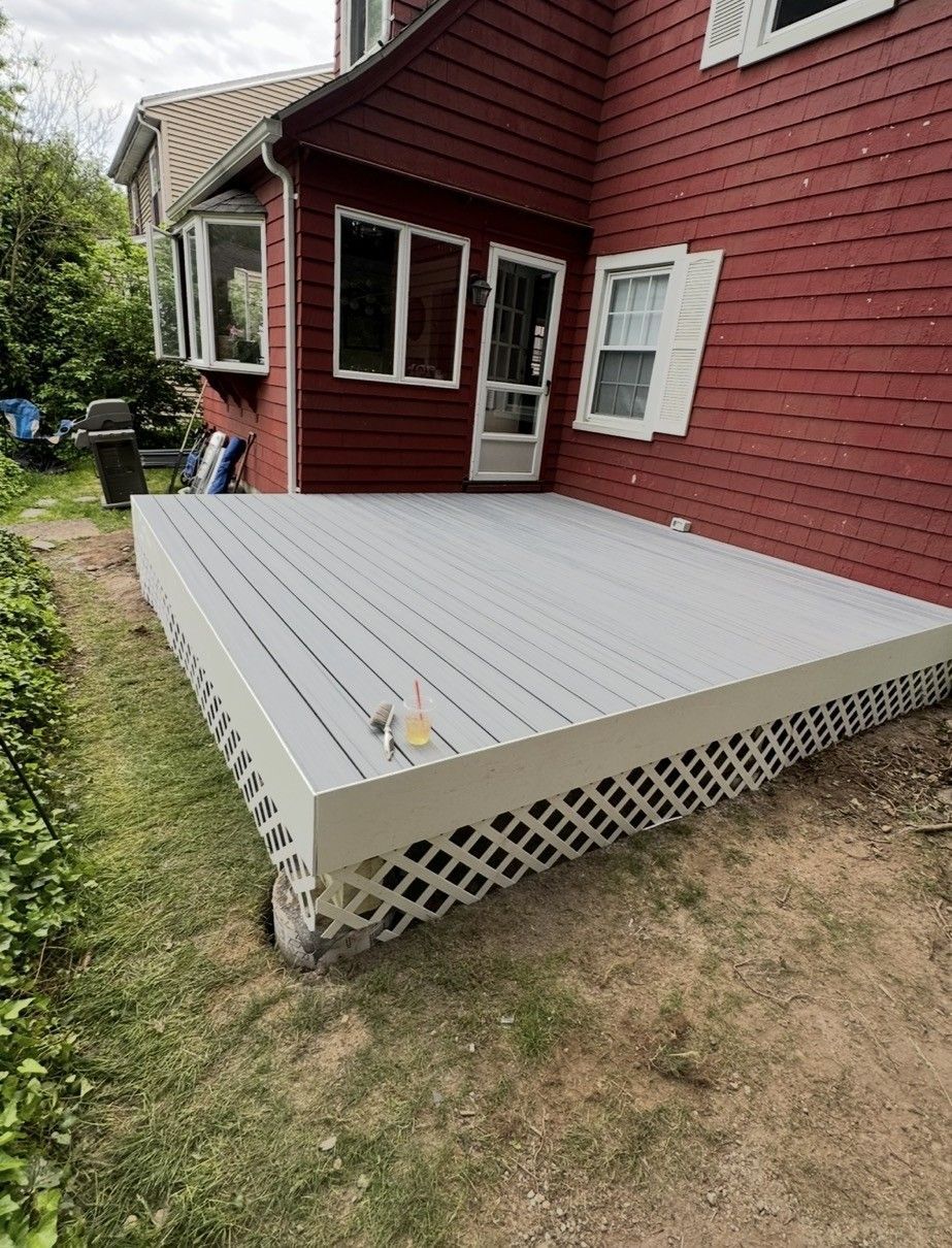 Gray wooden deck attached to a red house, with lattice skirting and a grassy yard.