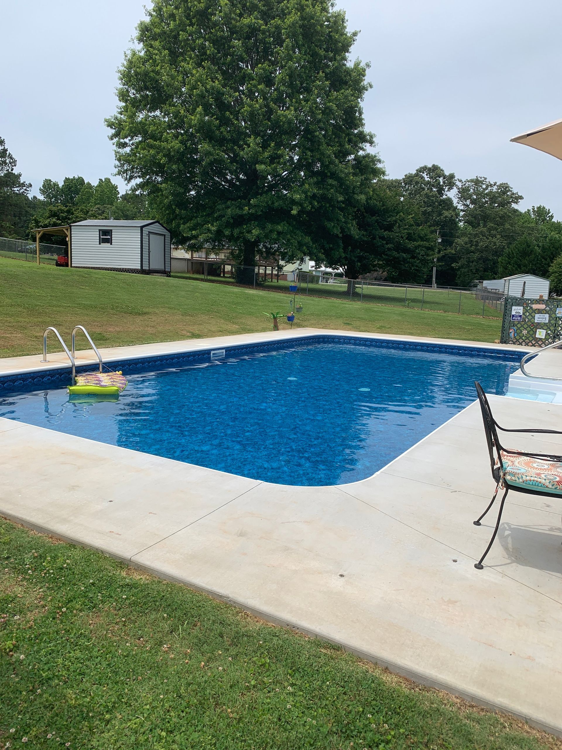 A large swimming pool with a chair and umbrella in front of it