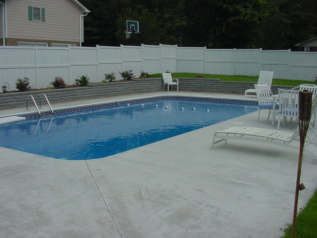 A large swimming pool surrounded by chairs and a white fence