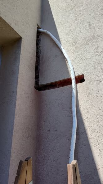 Un tubo aislante blanco se curva a lo largo de una pared de color canela, sostenido por un soporte