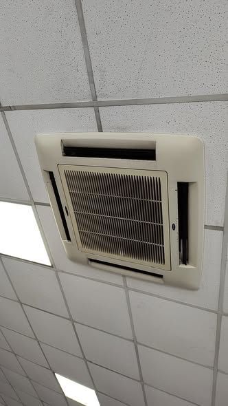 Unidad de aire acondicionado de techo con marco rectangular de color blanco y rejilla de ventilación de rejilla oscura.