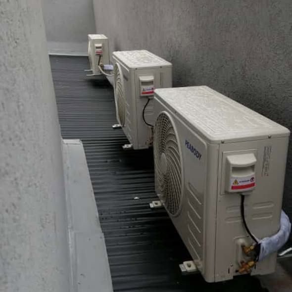 Tres unidades de aire acondicionado exteriores montadas sobre una superficie negra contra paredes grises.
