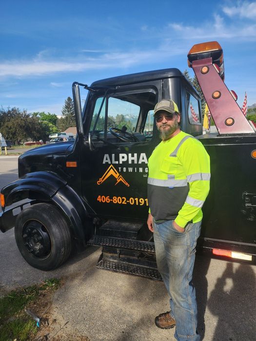 Tow truck driver in neon jacket standing beside a black tow truck with ALPHA signage outdoors