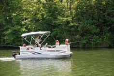 Pontoon boat with people fishing on a lake, green trees in the background.