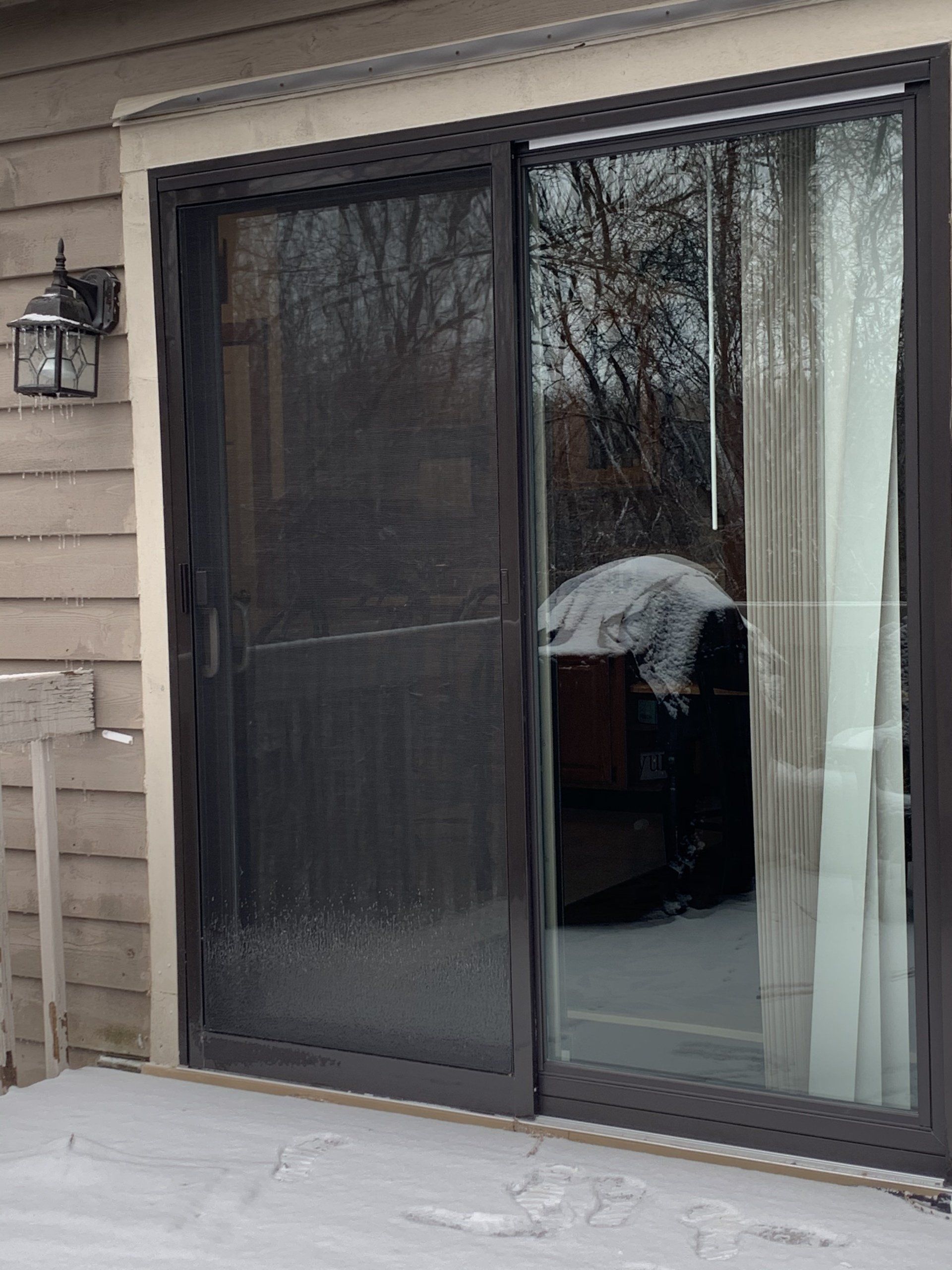 Sliding glass door with a screen, in a snowy outdoor setting.