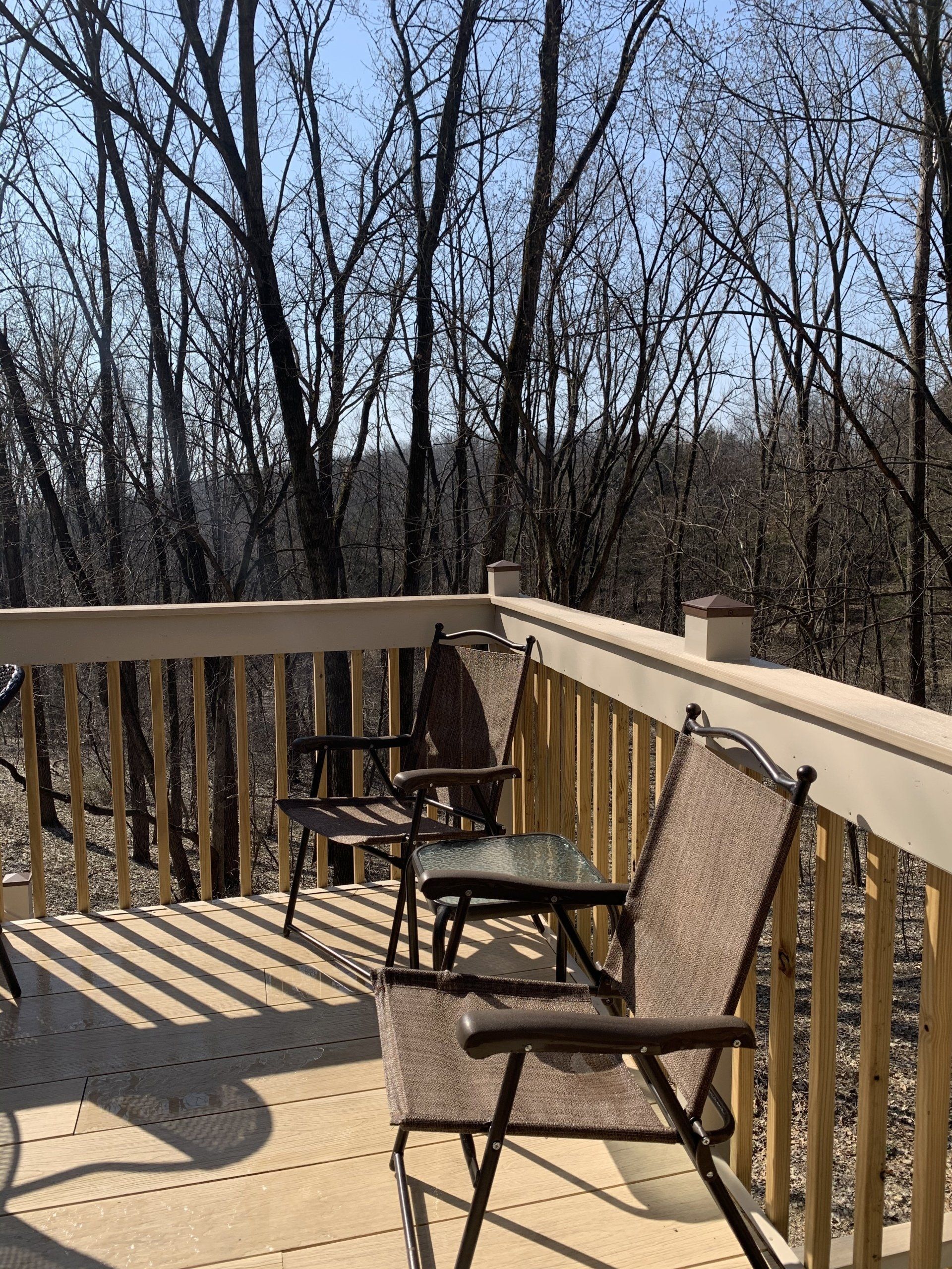 Two chairs and a small table on a wooden deck overlooking bare trees.