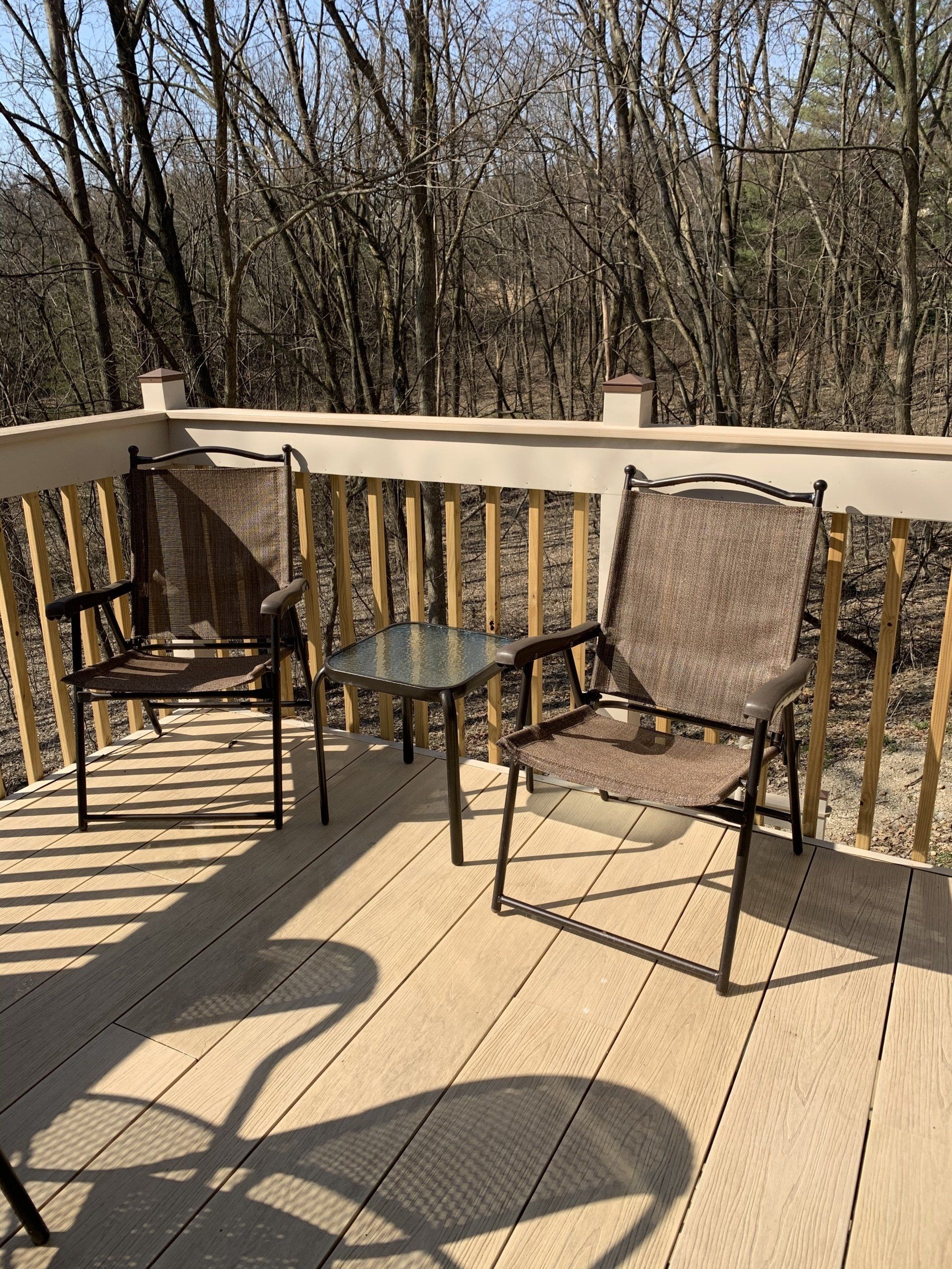 Two chairs and small table on wooden deck, trees in background.