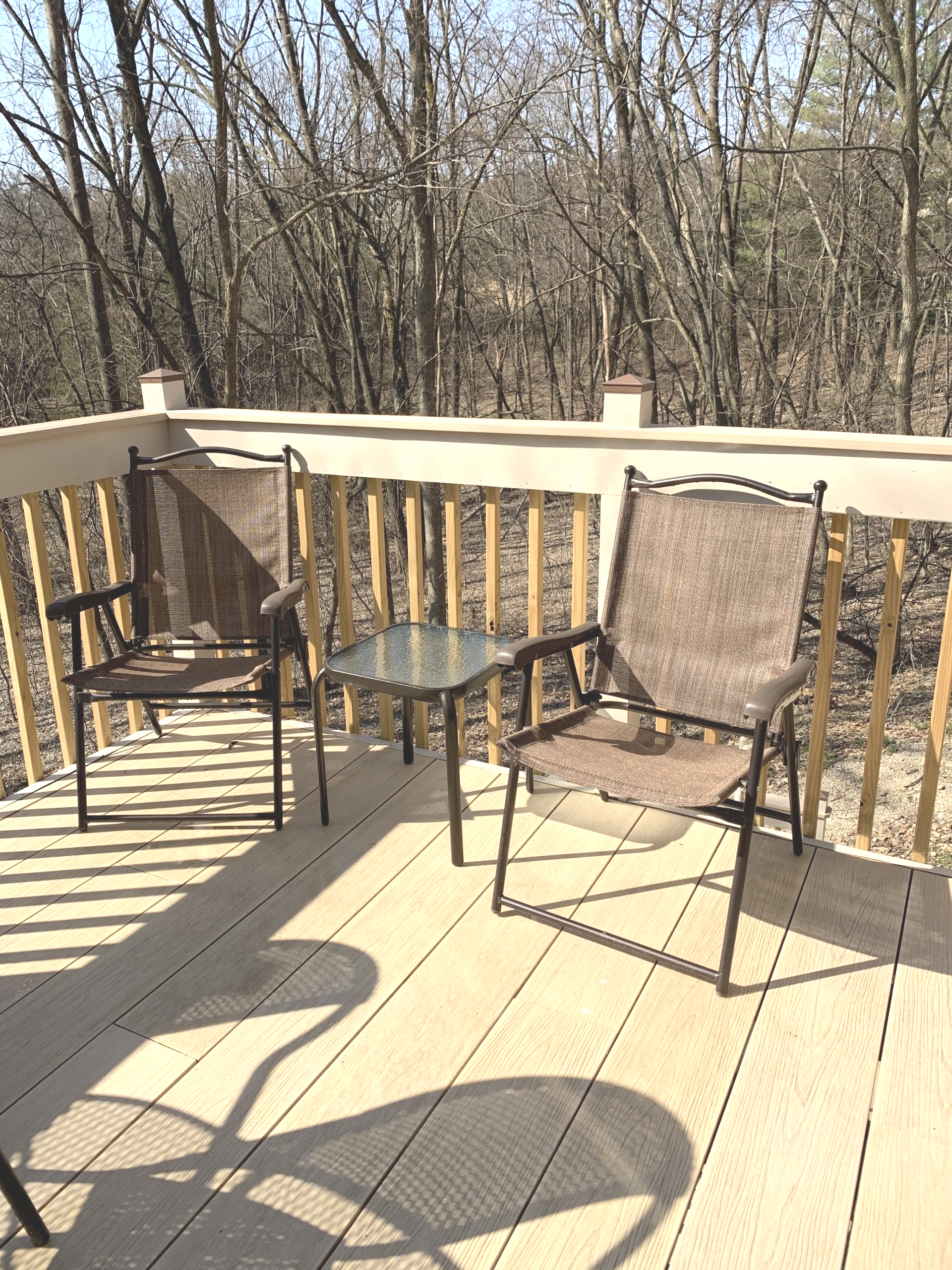 Two chairs and a small table on a wooden deck, trees in the background.