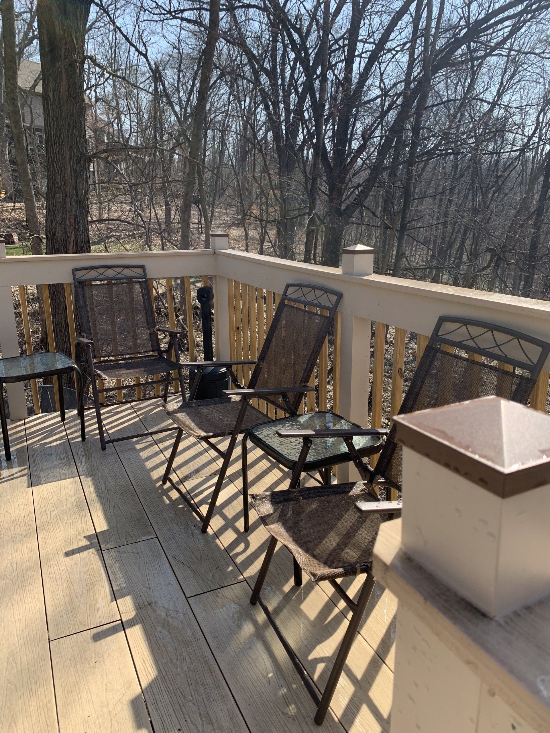 Patio with three chairs and a small table on a deck overlooking a wooded area.