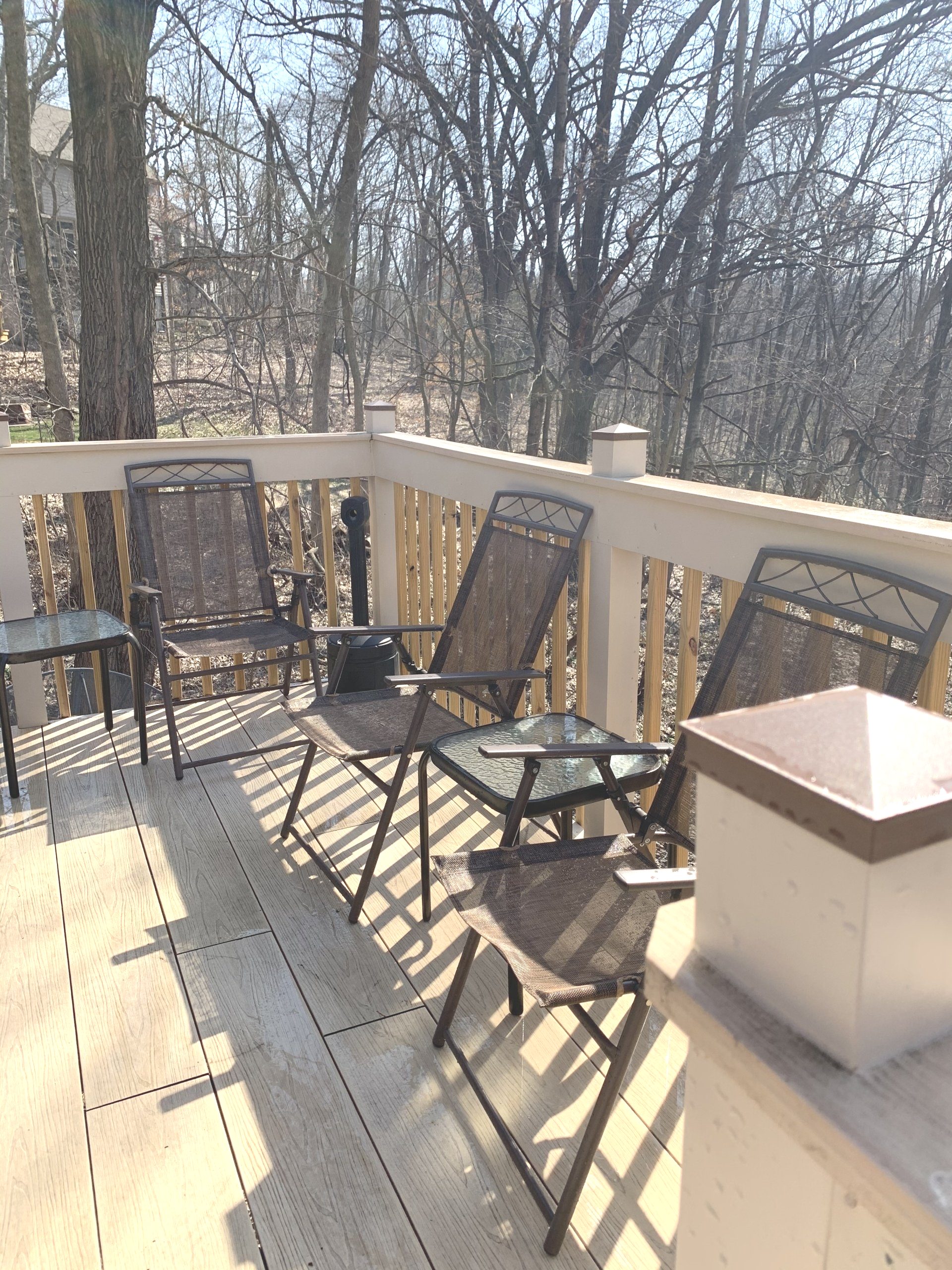 Deck with three metal chairs and a small table, overlooking a wooded area.