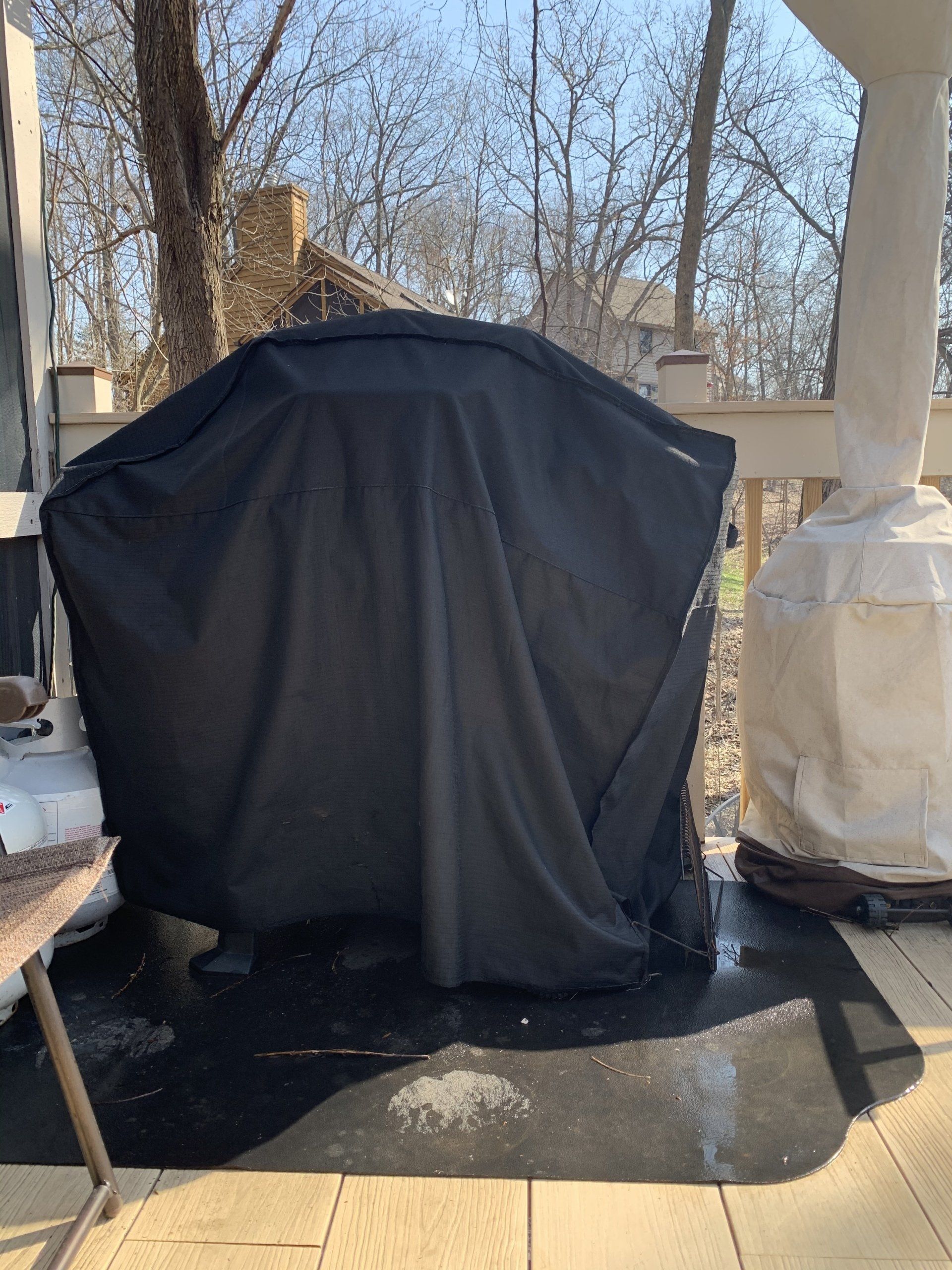 A black grill cover on a deck, with trees in the background under a sunny sky.