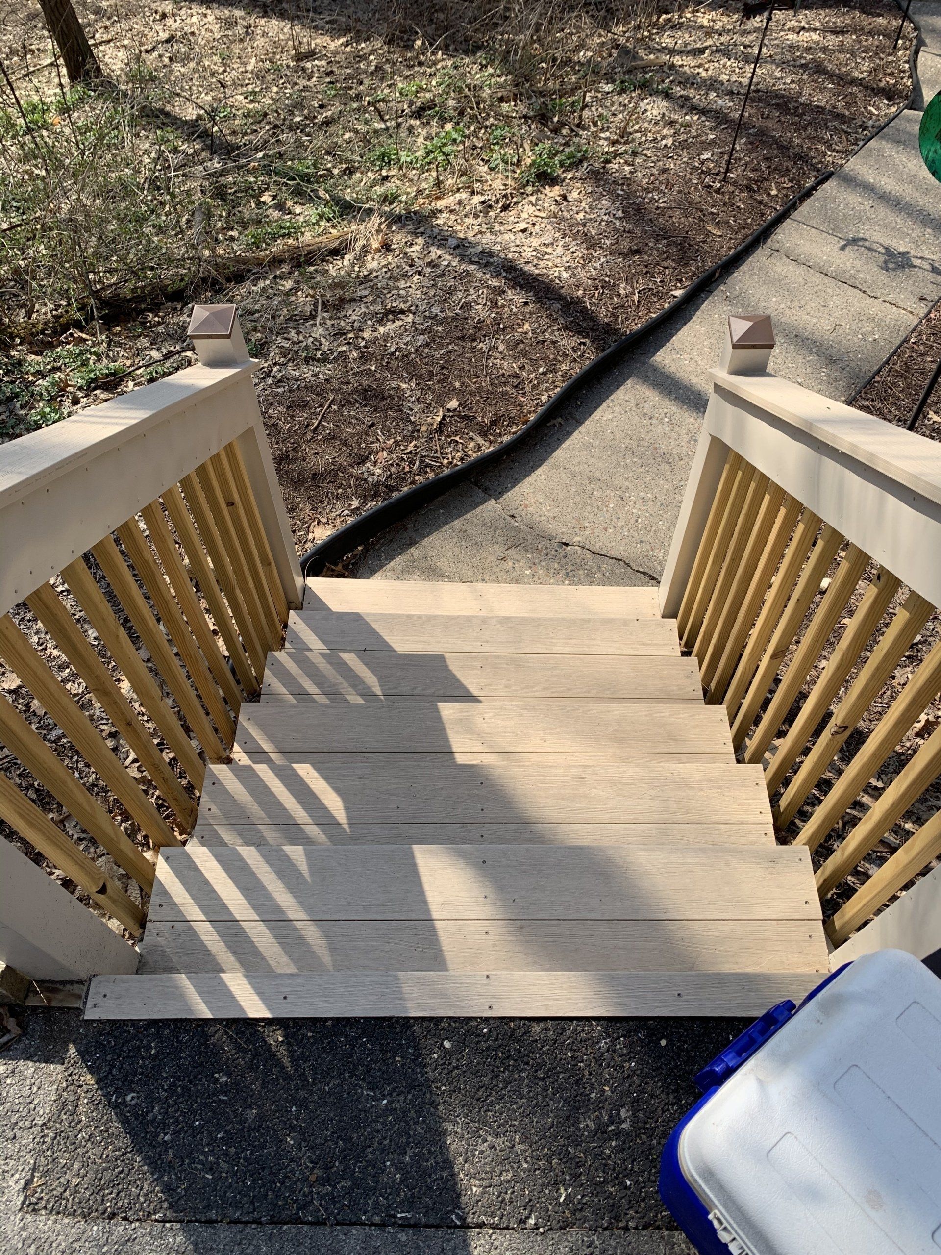 Wooden stairs leading down, with railings. Sidewalk and mulch in background.