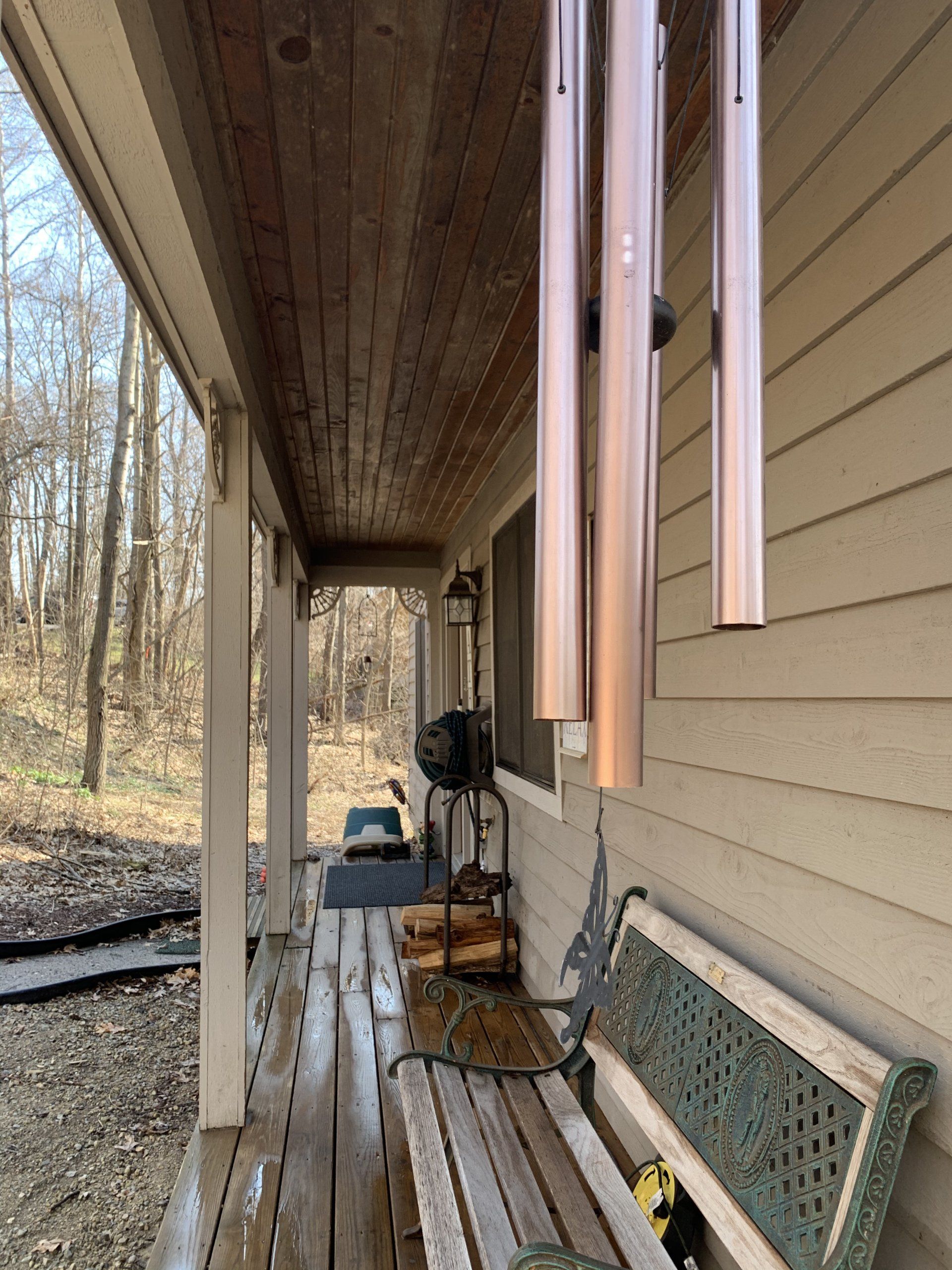 Covered porch with wind chimes, bench, and wooden ceiling. Exterior view.