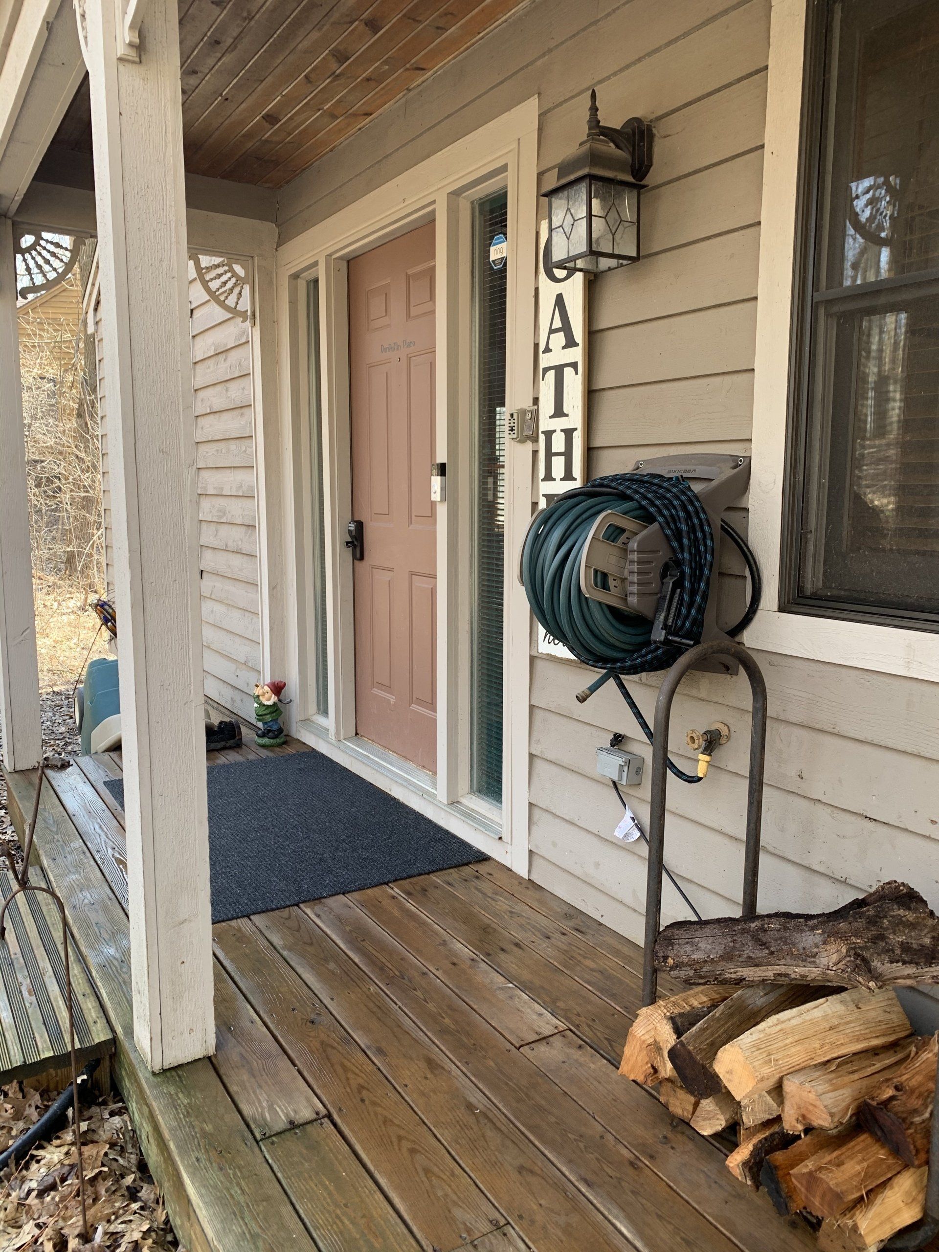 Front porch with pink door, hose, firewood, and