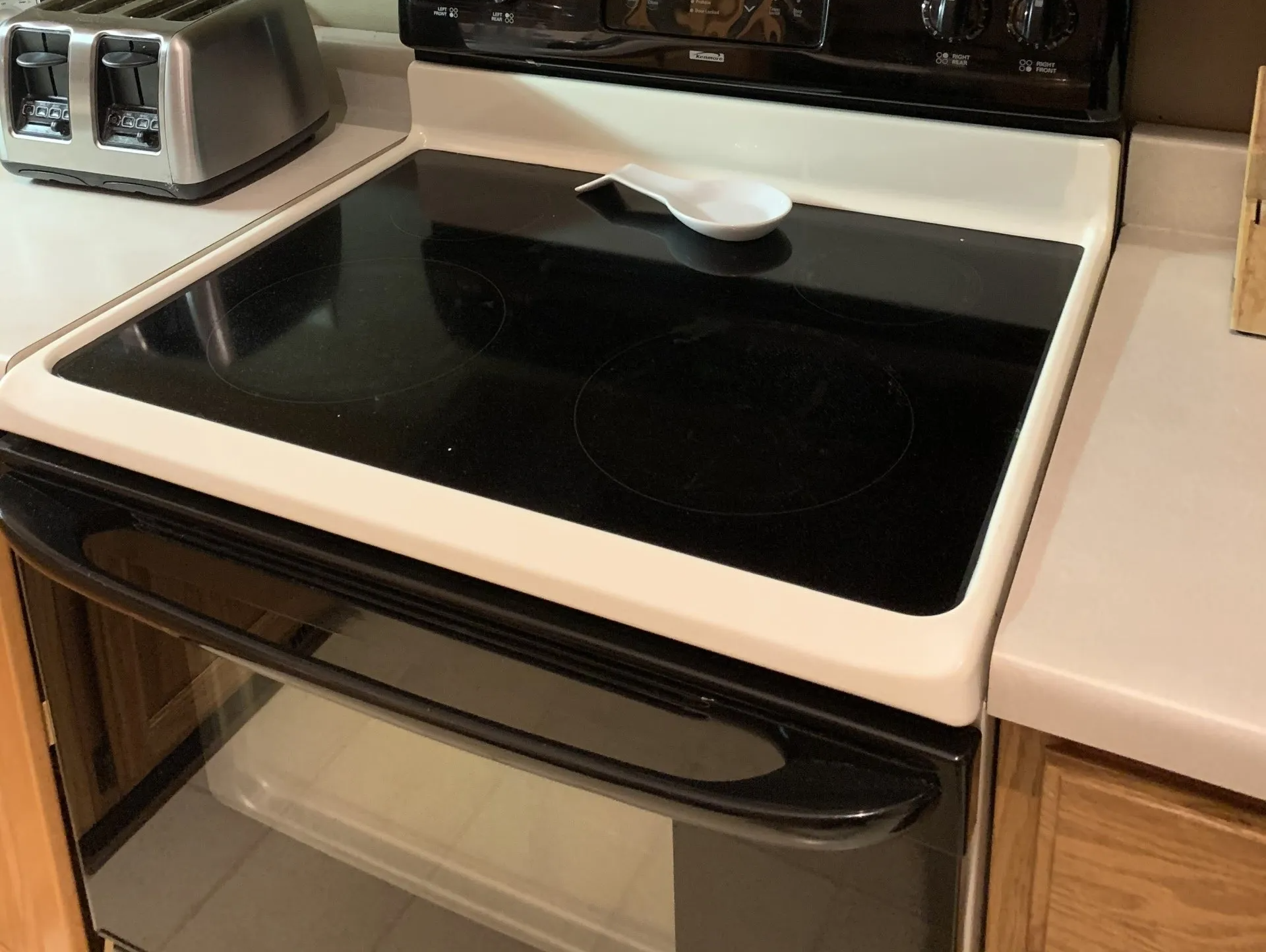 Black electric stovetop with white trim, a white spoon, and a toaster.