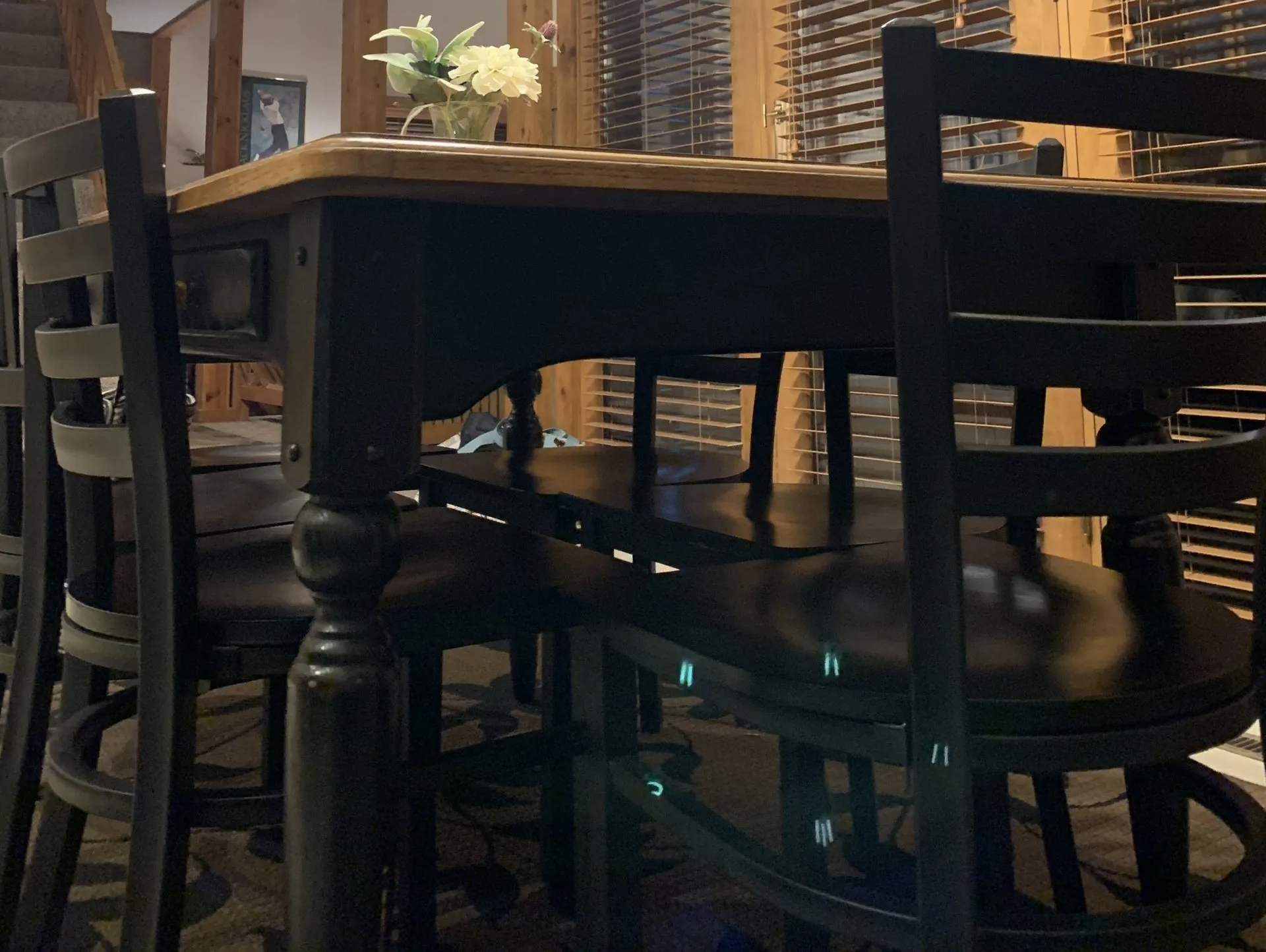 Black table and chairs in a dining area. Wooden table with flowers on top and wine racks in the background.